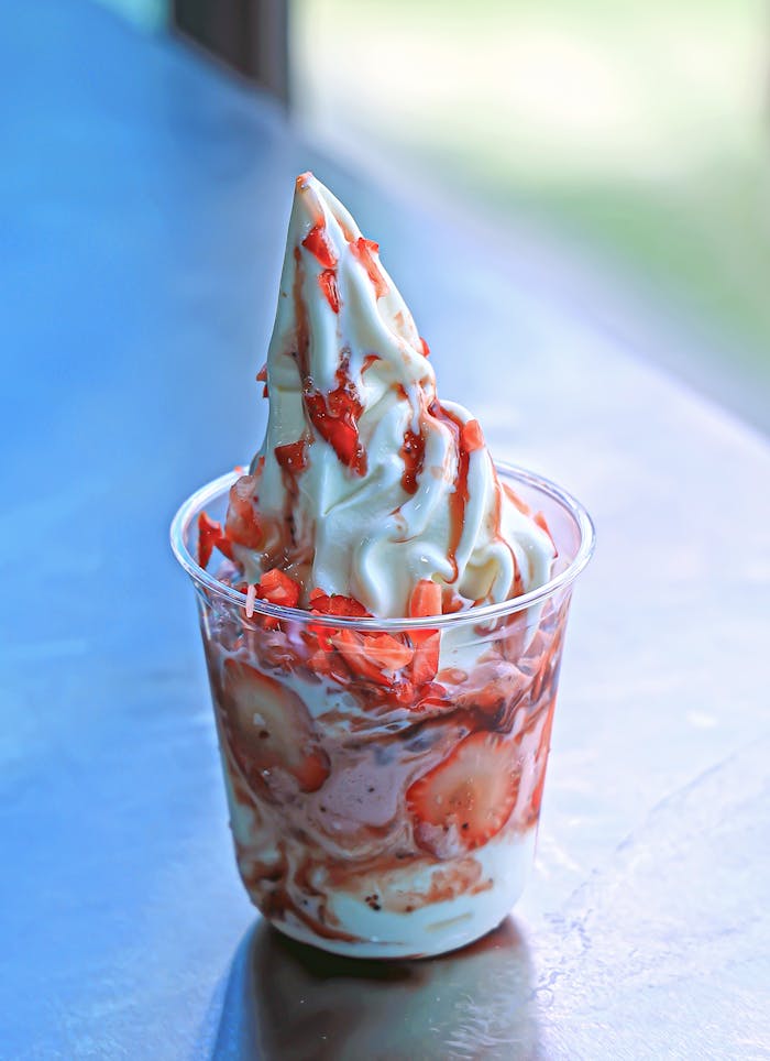 Creamy soft serve ice cream with fresh strawberries in a clear cup on a sunny day.