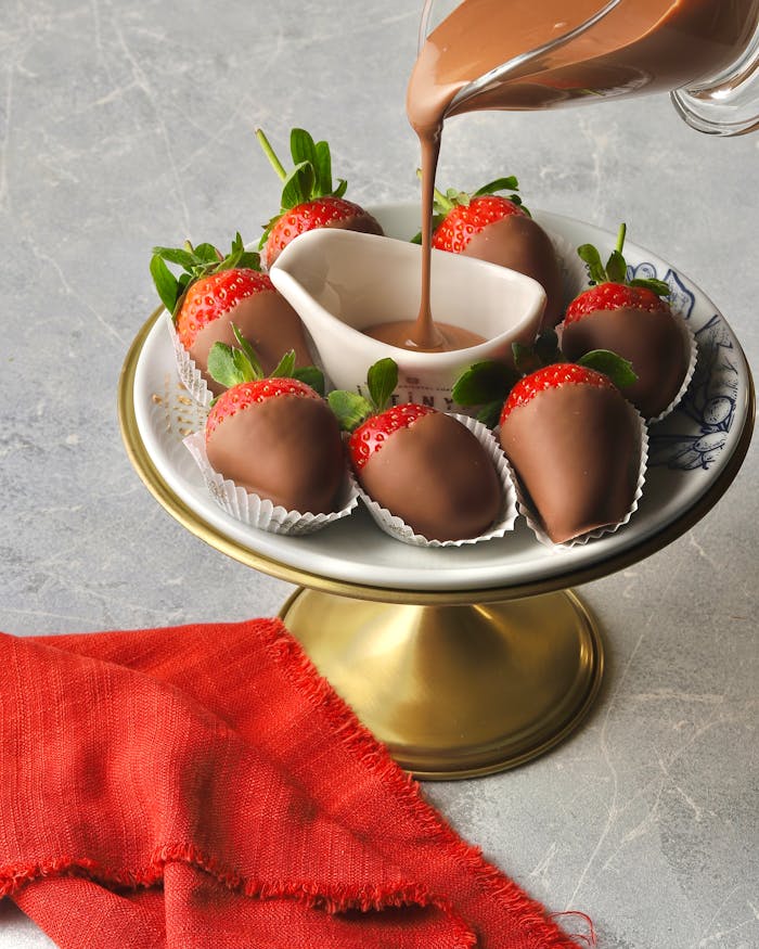 Indulgent chocolate-covered strawberries on a gold stand with pouring chocolate.