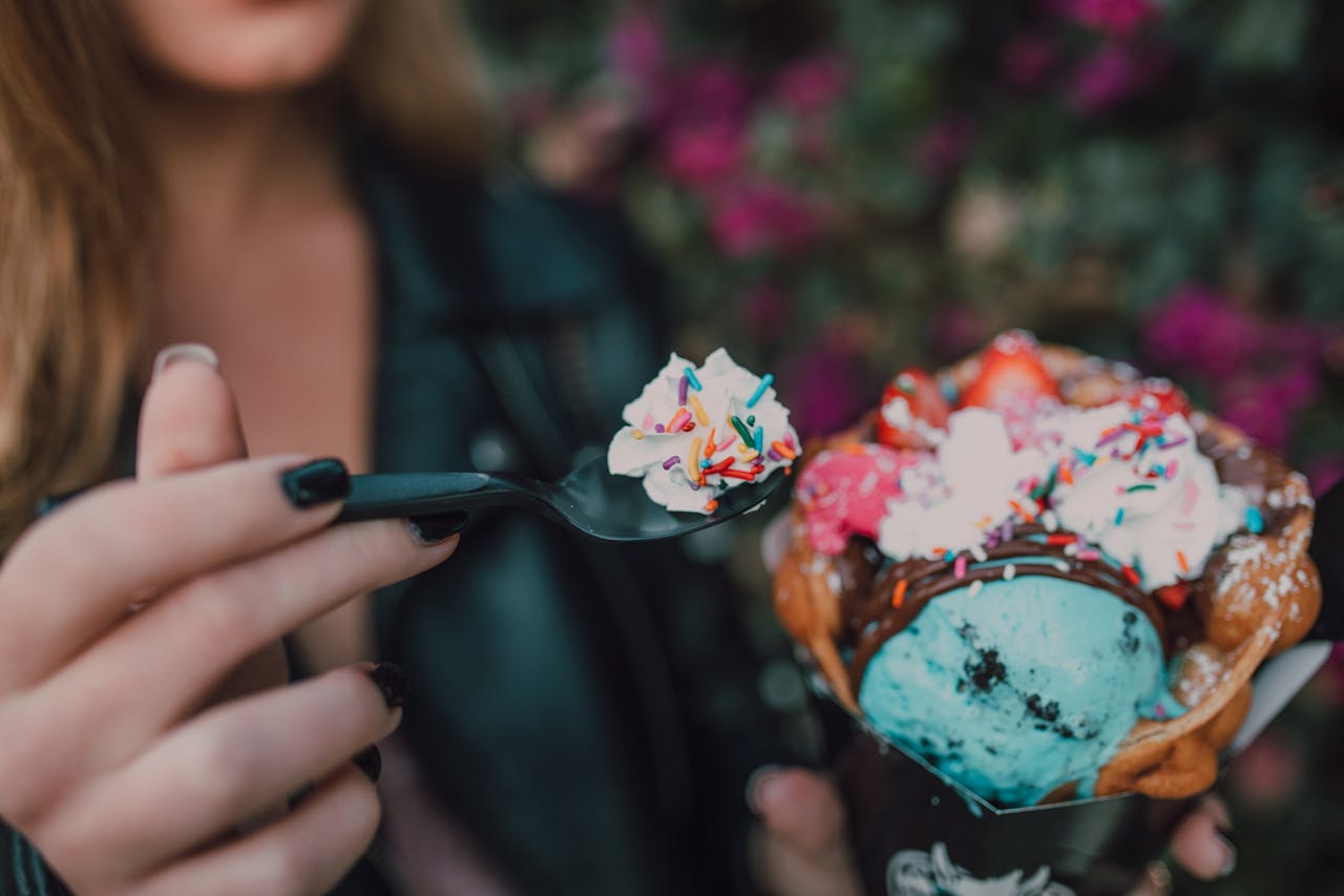 about-03 Close-up of a vibrant ice cream dessert with waffle cone and sprinkles, held by a woman.