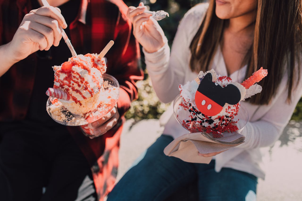 Two people enjoying vibrant ice cream sundaes outdoors on a sunny day.