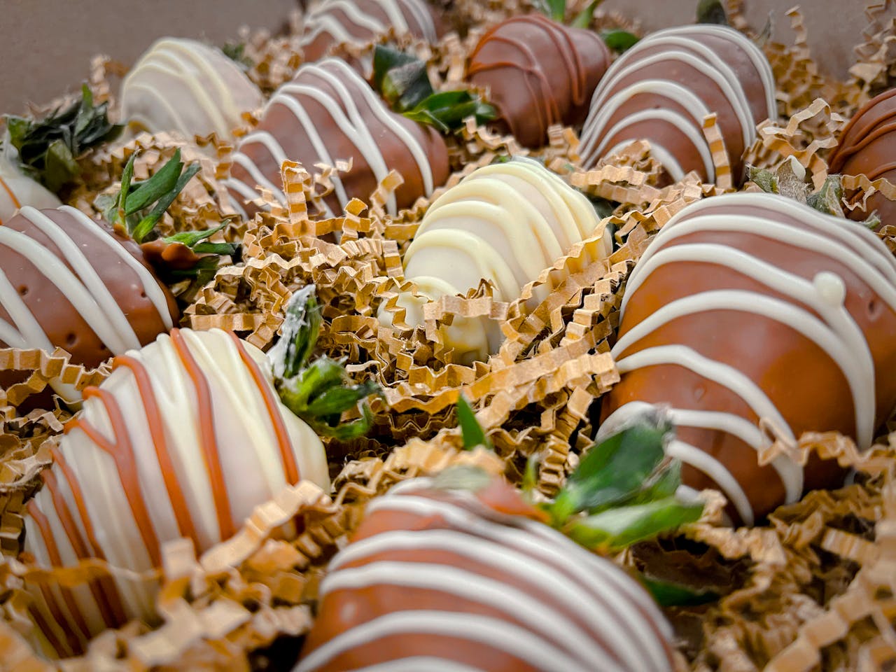 about-04 Close-up of assorted chocolate-dipped strawberries with drizzled patterns on a bed of crinkle paper.