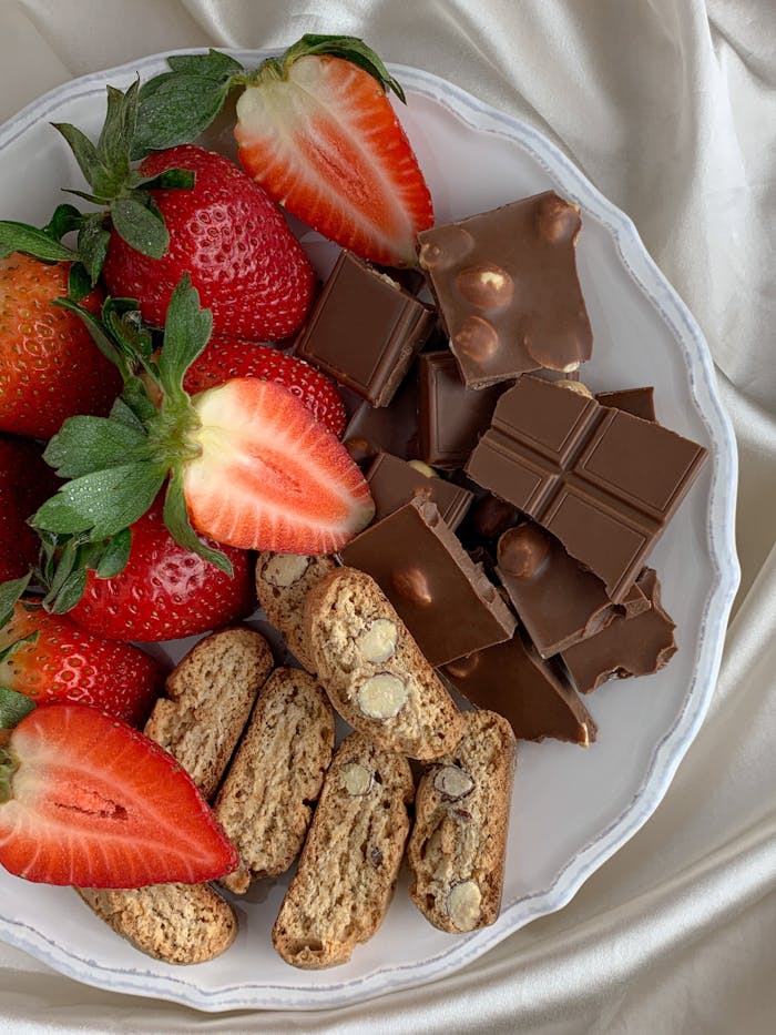 A tempting flat lay of strawberries, chocolate, and biscotti on a white plate.